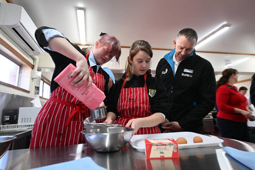 Tamworth High School students Jemma Bazal and Isabella Coe start their cupcakes under the watchful eye of one of the event judges, TAFE team leader for tourism and experience services Matthew McAllister. Pictyre by Gareth Gardner