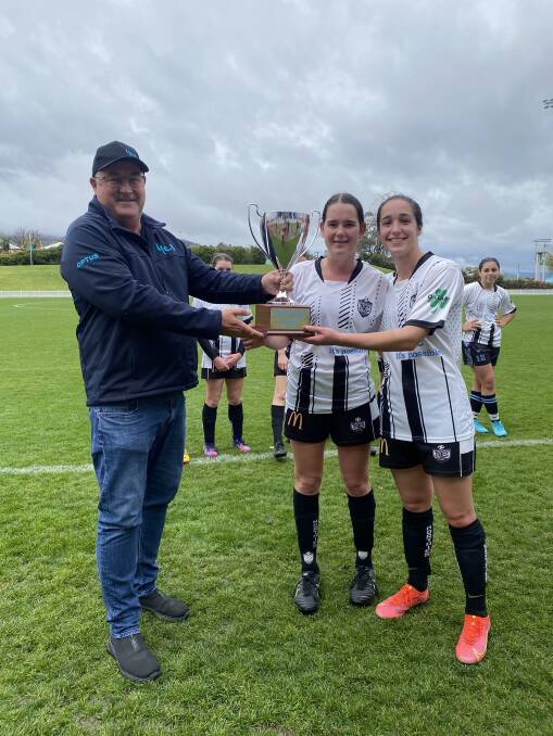 Optus representative Eric Doherty presents the inaugural Optus Cup to departing North Companions pair Ellen Carter (left) and Sami Wilkie (right).