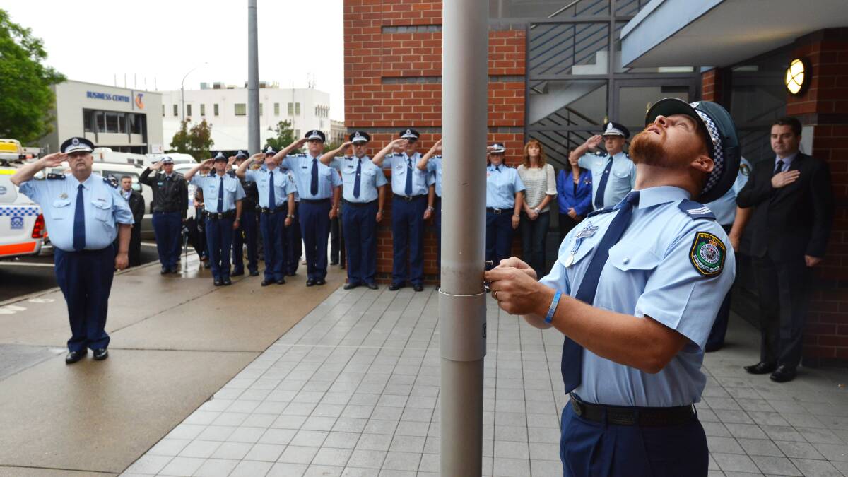 Tamworth police Sergeant Josh McKenzie lowers the flag to half mast at the service to mark the first anniversary of David Rixon's death. Photo:Barry Smith 020313BSA23